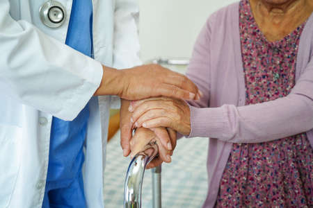 Doctor help Asian elderly woman disability patient walk with walker in nursing hospital, medical concept.の写真素材