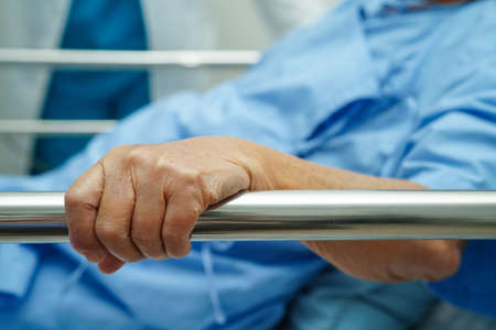 Asian elder senior woman patient holding bed rail while lie down with hope waiting her family in hospital.の写真素材
