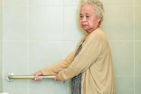 Asian elderly old woman patient use toilet support rail in bathroom, handrail safety grab bar, security in nursing hospital.の写真素材