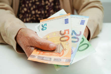 Retired elderly woman holding Euro banknotes money and worry about monthly expenses and treatment fee payment.の写真素材