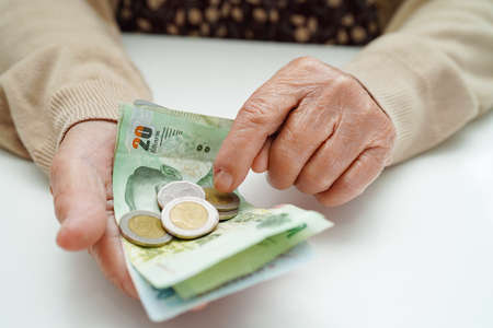 Retired elderly woman counting coins money and worry about monthly expenses and treatment fee payment.の写真素材