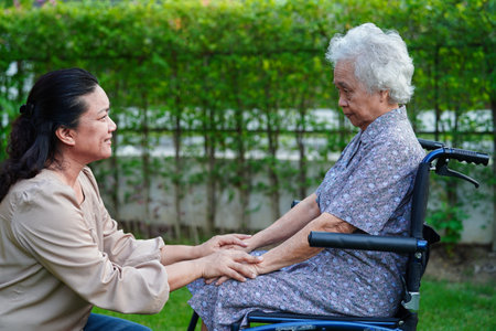 Caregiver help Asian elderly woman disability patient sitting on wheelchair in park, medical concept.の写真素材