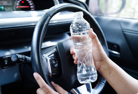 Asian woman driver hold cold water for drink in car, dangerous and risk an accident.の写真素材