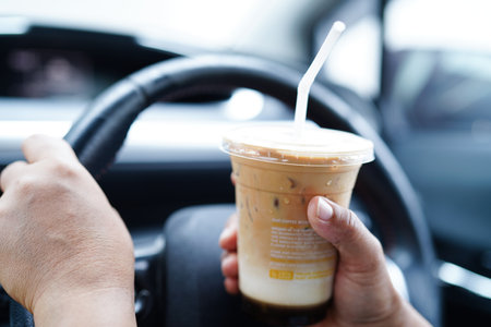 Bangkok, Thailand - May 15, 2022 Asian woman driver hold ice coffee cup for drink in car, dangerous and risk an accident.の写真素材