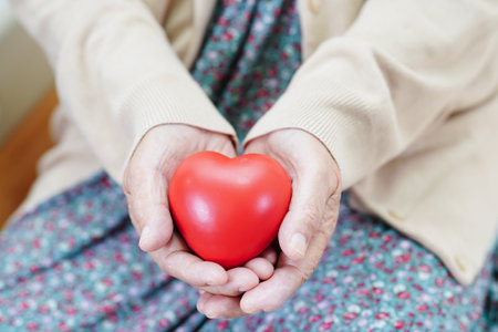 Asian elder senior woman patient holding red heart in hospital.