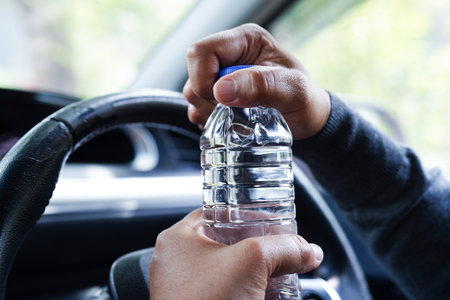Asian woman driver hold cold water for drink in car, dangerous and risk an accident.の写真素材
