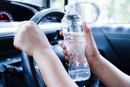 Asian woman driver hold cold water for drink in car, dangerous and risk an accident.の写真素材