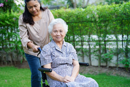 Caregiver help Asian elderly woman disability patient sitting on wheelchair in park, medical concept.の写真素材