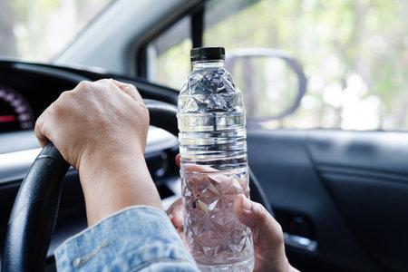 Asian woman driver hold cold water for drink in car, dangerous and risk an accident.の写真素材