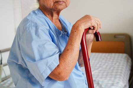 Asian elderly disability woman patient holding walking stick in wrinkled hand at hospital.の写真素材
