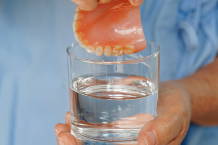Asian senior woman patient clean teeth denture in a glass with solution for chew food.