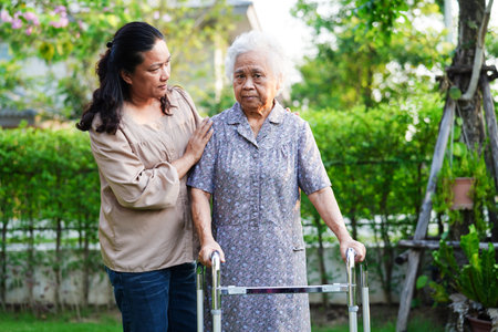 Caregiver help Asian elderly woman disability patient walk with walker in park, medical concept.の写真素材