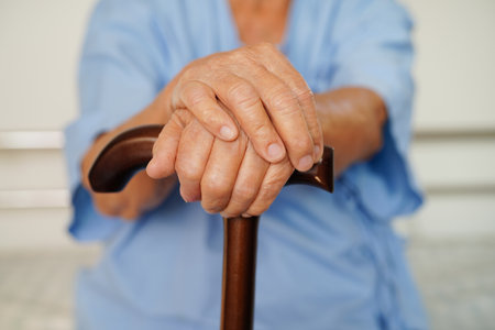 Asian elderly disability woman patient holding walking stick in wrinkled hand at hospital.の写真素材