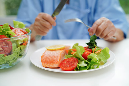 Asian elderly woman patient eating salmon stake and vegetable salad for healthy food in hospital.の写真素材
