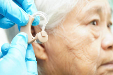 Doctor install hearing aid on senior patient ear to reduce hearing loss problem.の写真素材