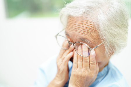 Asian senior woman wearing eyeglasses reduce headache and eyestrain suffer at home care service.の写真素材