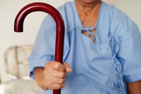 Asian elderly disability woman patient holding walking stick in wrinkled hand at hospital.の写真素材