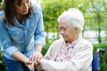 Caregiver help Asian elderly woman disability patient sitting on wheelchair in park, medical concept.の写真素材