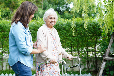Caregiver help Asian elderly woman disability patient walk with walker in park, medical concept.の写真素材
