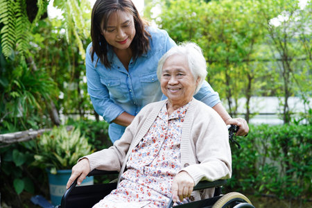 Caregiver help Asian elderly woman disability patient sitting on wheelchair in park, medical...