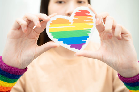 Asian woman holding LGBT heart with rainbow flag.