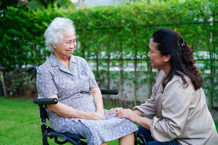 Caregiver help Asian elderly woman disability patient sitting on wheelchair in park, medical.の写真素材