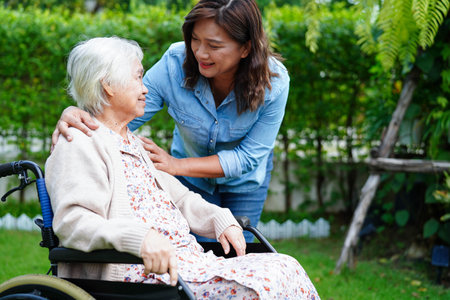 Caregiver help Asian elderly woman disability patient sitting on wheelchair in park, medical.の写真素材