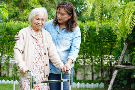 Caregiver help Asian elderly woman disability patient walk with walker in park, medical concept.の写真素材