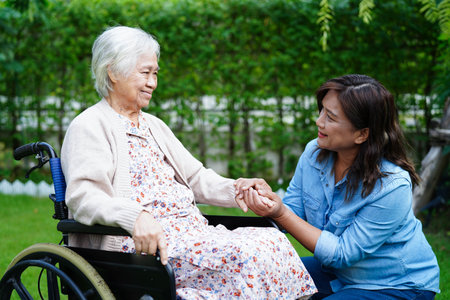 Caregiver help Asian elderly woman disability patient sitting on wheelchair in park, medical.の写真素材