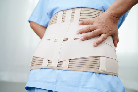 Asian senior pain back wearing elastic support belt with walker.