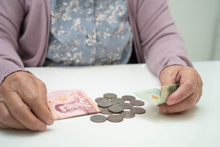 Retired elderly woman counting coins money with piggy bank and worry about monthly expenses and treatment fee payment.の写真素材