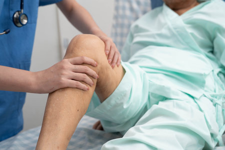 Doctor checking Asian elderly woman patient with scar knee replacement surgery in hospital.