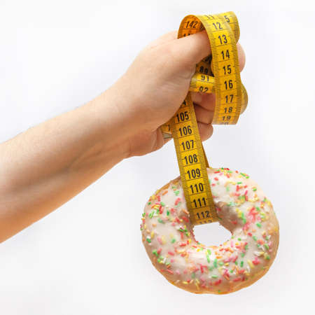 Woman's hand holds a measuring tape on which hangs a sweet donut. White background. Side view.