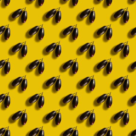 A repeating pattern of two eggplants with harsh shadows is set against a yellow backgroundの写真素材