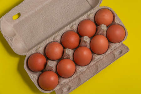 Cardboard package with fresh red eggs on a yellow background. View from above. Diet.
