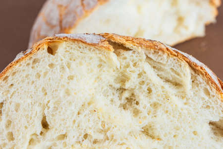 A slice of white fresh crispy bread on a brown background.