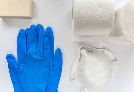 COVID-19. On a white background are personal hygiene products during the epidemic. These are blue disposable medical gloves, soap, mask, toilet paper.の写真素材