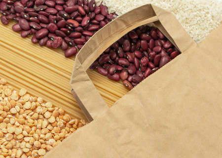 On a flat surface is a brown paper bag. Nearby are dry products from the emergency stock: peas,...