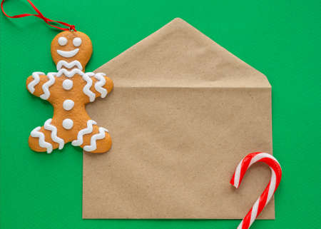 Christmas card mockup. Blank craft brown envelope, gingerbread man, lollipop on green background. New Year and Christmas concept. Top view, flat lay.の写真素材