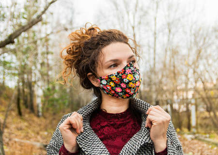 A beautiful brown-haired woman in a mask is in the park during the coronavirus period.