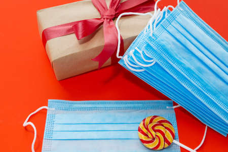 Creative concept of Christmas and New Year during coronavirus. On a red background, there is a gift, a lollipop and blue medical masks.の写真素材