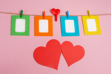 Colored photo frames are attached to the rope with clothespins. Pink background decorated with red hearts. Valentine's Day.の写真素材