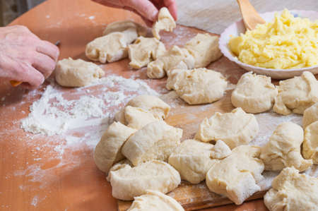 A woman cuts raw dough into small pieces for homemade baking stuffed with mashed potatoes. Home hobby.の写真素材
