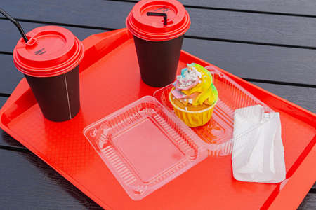 Rainbow cake and two cups of coffee stand on a tray in an outdoor cafe.