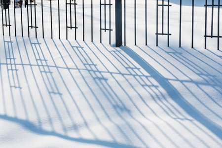 A beautiful patterned shadow from a metal fence is on the white snow.の写真素材