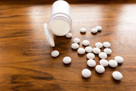 White pills and an empty white bottle lie on the table surface.