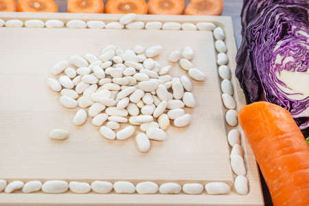 Raw white beans, cabbage, carrots are on the table next to a wooden board. Ingredients for a vegetarian meal. There is room for text.の写真素材