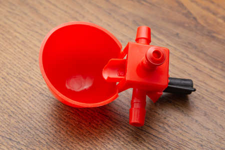 Red, small, plastic, round drinking bowl for chickens on a wooden background.