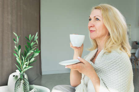 Happy middle-aged blonde in the morning drinks coffee or tea, holds a cup in her hand.の写真素材