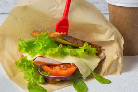Sandwich with cheese, ham and salad, takeaway coffee in a paper cup. The concept of food delivery, lunch in the office.の写真素材